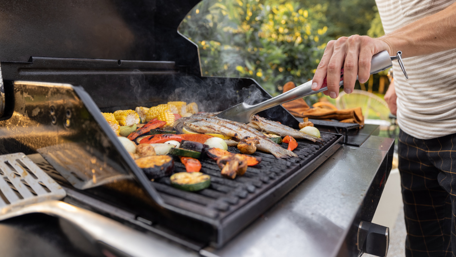 People,Grilling,Fish,And,Corn,On,A,Modern,Grill,Outdoors Use a stiff wire brush to clean your grill’s grates before inviting the neighbors over for a backyard feast.